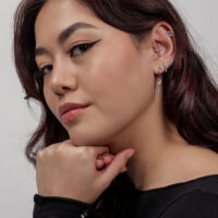 Frau mit silbernen Ohrpiercings, darunter ein Kristallblatt, auf grauem Hintergrund