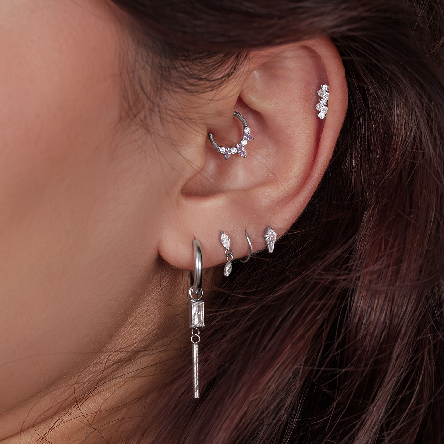 Silberne Ohrpiercings mit Kristallen Nahaufnahme eines Ohres mit mehreren silbernen Piercings, einige mit Kristallen besetzt