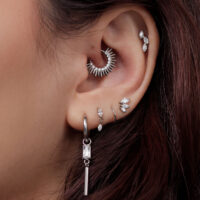 Nahaufnahme eines Ohres mit mehreren silbernen Ohrringen, darunter ein auffälliger spitzer Ring im inneren Ohrbereich.