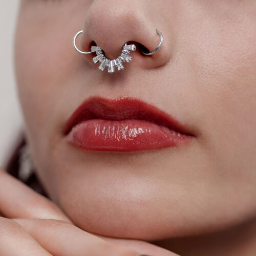 Nahaufnahme eines silbernen Septum Clickers mit Kristallen in einer Nase, rote Lippen sichtbar