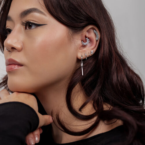 Frau mit mehreren silbernen Ohrringen, Mondmotiv und Kugeln im Ohr auf grauem Hintergrund